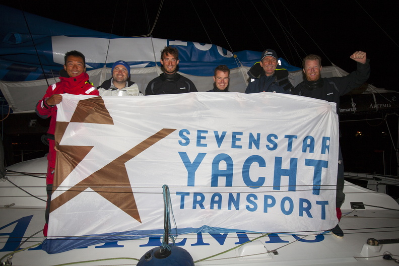 Brian Thompson and the crew of Artemis - Team Endeavour pose behind the sponsor race flag