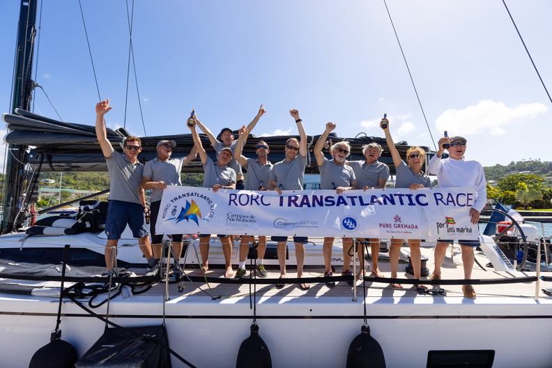 The crew of Jean Pierre Dreau's Mylius 60 Lady First 3 gather on deck with the official race banner