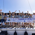 The crew of Jean Pierre Dreau's Mylius 60 Lady First 3 gather on deck with the official race banner